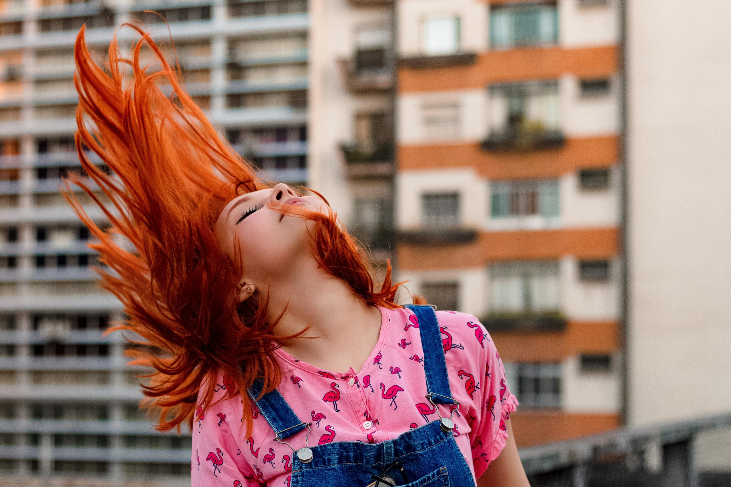 Vibrant portrait of a woman flipping her red hair outdoors. Captivating, energetic, and colorful.